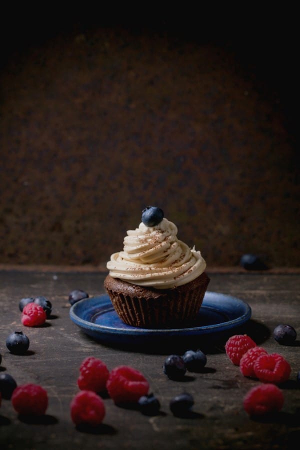 Chocolate cupcake with butter coffee cream and fresh berries over dark background