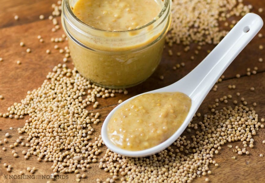 Homemade Sweet Hot Mustard in a small jar and in a large spoon with mustard seeds around them.