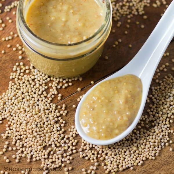 Homemade hot mustard on a large spoon beside a small jar of mustard with mustard seeds on the counter.