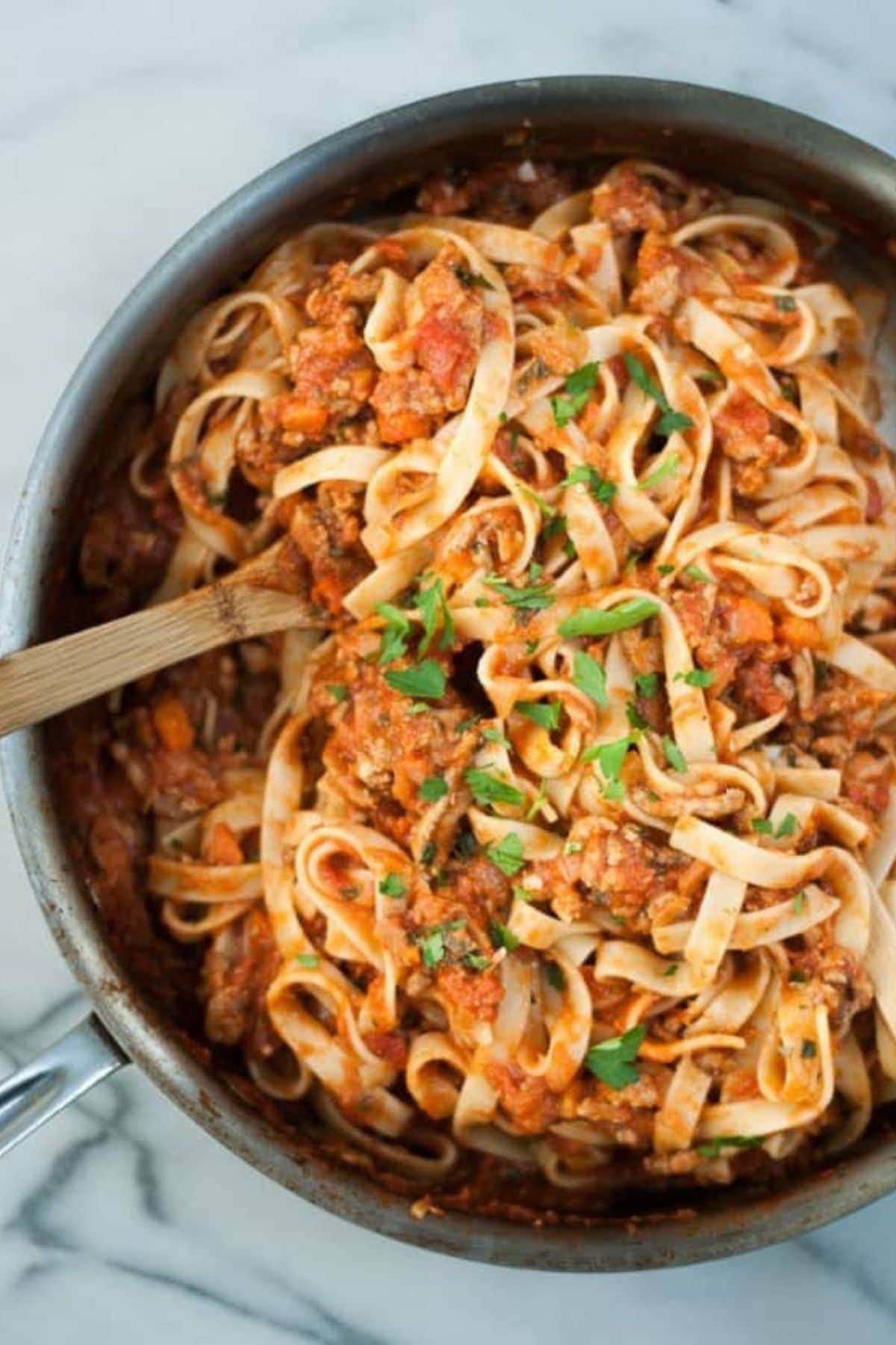 Sauce pan filled with fettucine turkey bolognese with a wooden spoon.