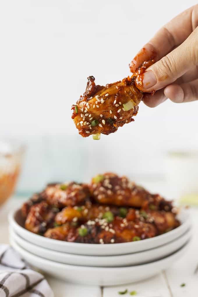 Hand holding a Korean Chicken wing over a platter of wings