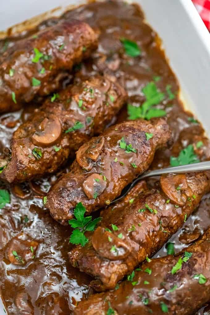 Beef Rouladen in a casserole dish with a silver serving spoon