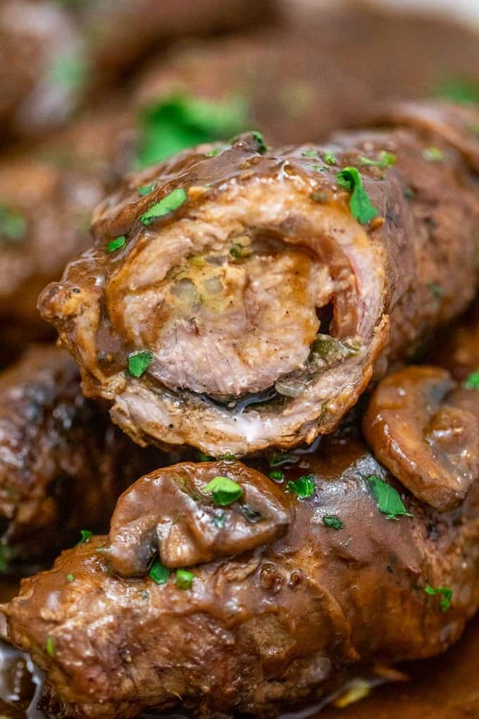 Beef rouladen roll cut in half, sitting on top of a full roll with mushroom gravy