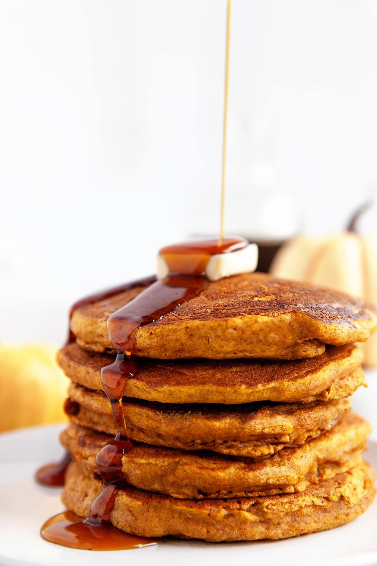 Five pumpkin pancakes stacked on top of each other, and  syrup being poured over the top. 