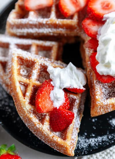 Showing a quarter of a waffle with strawberries and whipped cream.