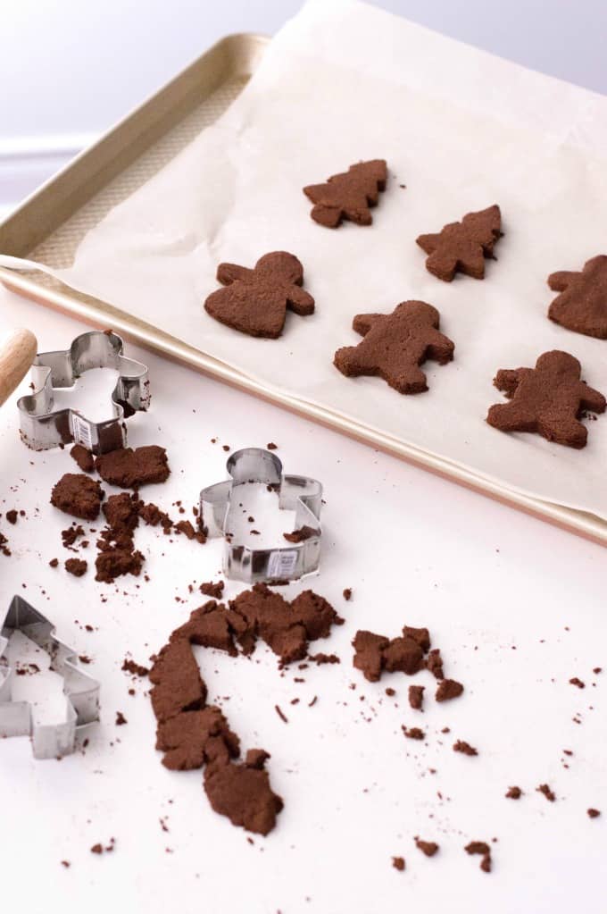 Cutout ornaments on a parchment lined cookie sheet with crumbs and cookie cutters