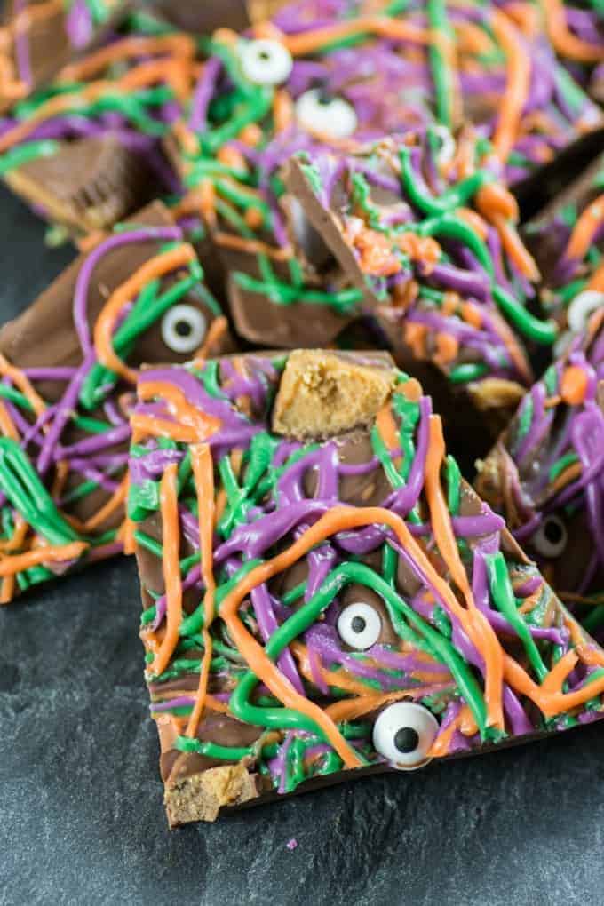 Purple, green and orange Halloween Bark with eyeballs and peanut butter cups on a slate board. 