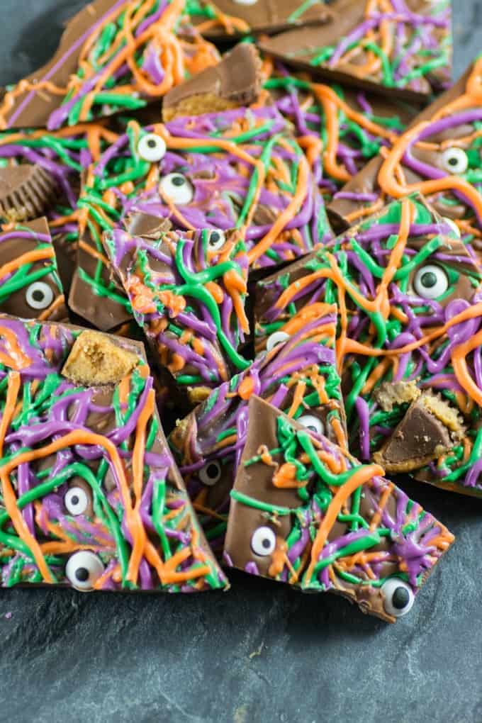 Purple, green and orange Halloween Bark with eyeballs and peanut butter cups on a slate board. 