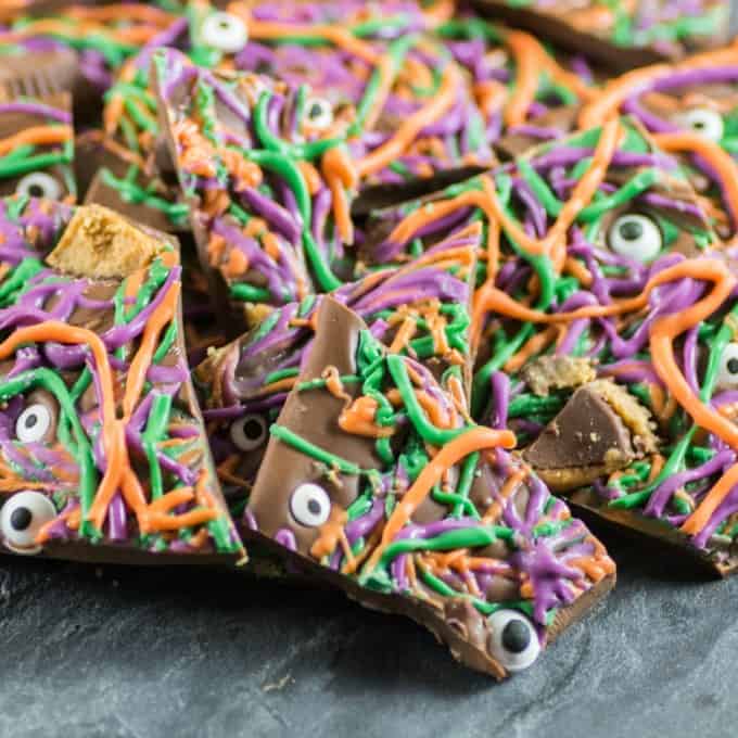 Purple, green and orange Halloween Bark with eyeballs and peanut butter cups on a slate board. 