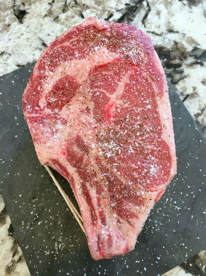 Prime rib with salt and pepper on a black slate cutting board