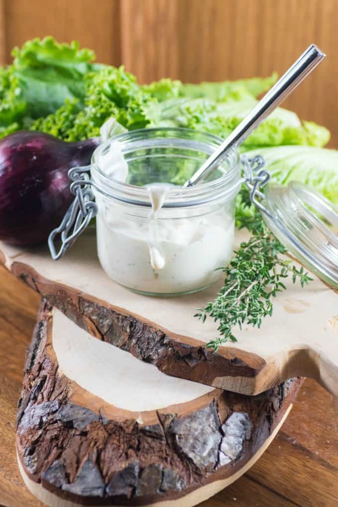 Buttermilk Ranch Dressing on a board with lettuce, red onion and thyme. 