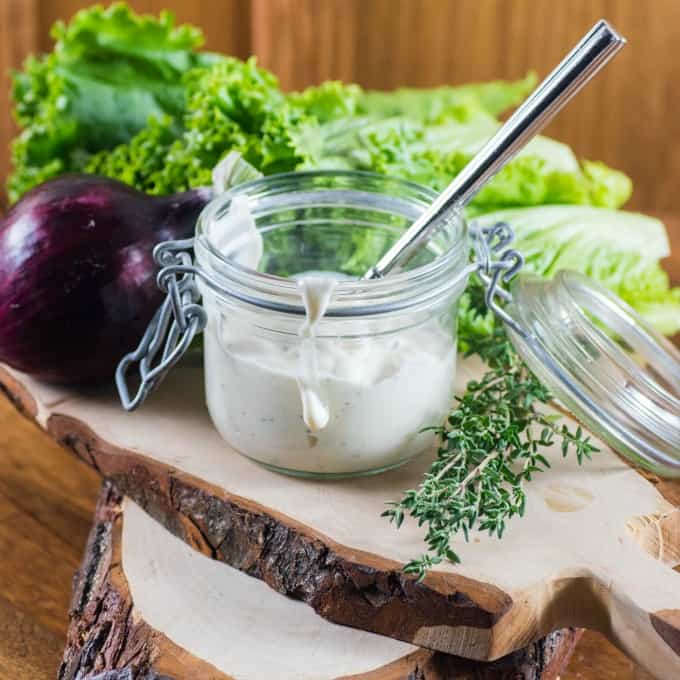 Buttermilk Ranch Dressing in a jar on a board with lettuce, red onion and thyme.