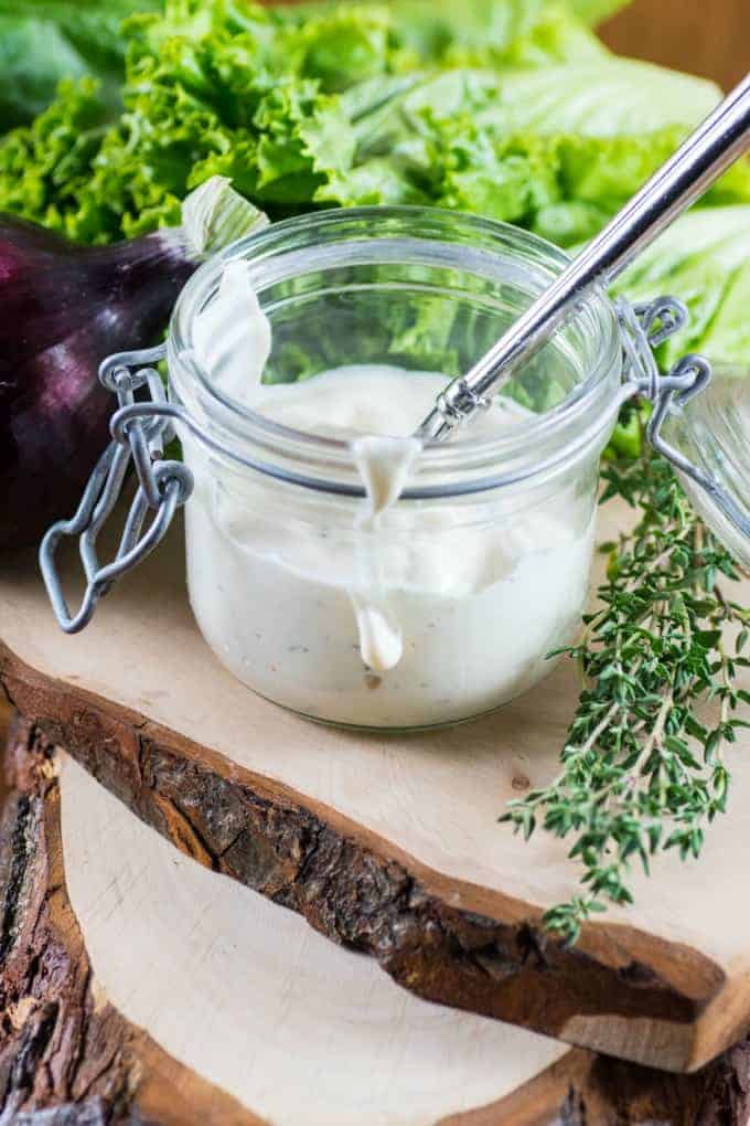 Buttermilk Ranch Dressing in a jar with a spoon in a board with vegetables. 