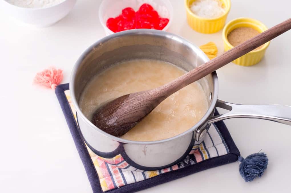 Fudge partially made in a pot on a pot warmer with a wooden spoon.