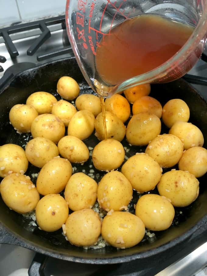 Creamer potatoes in a cast iron pan with beef stock being poured in