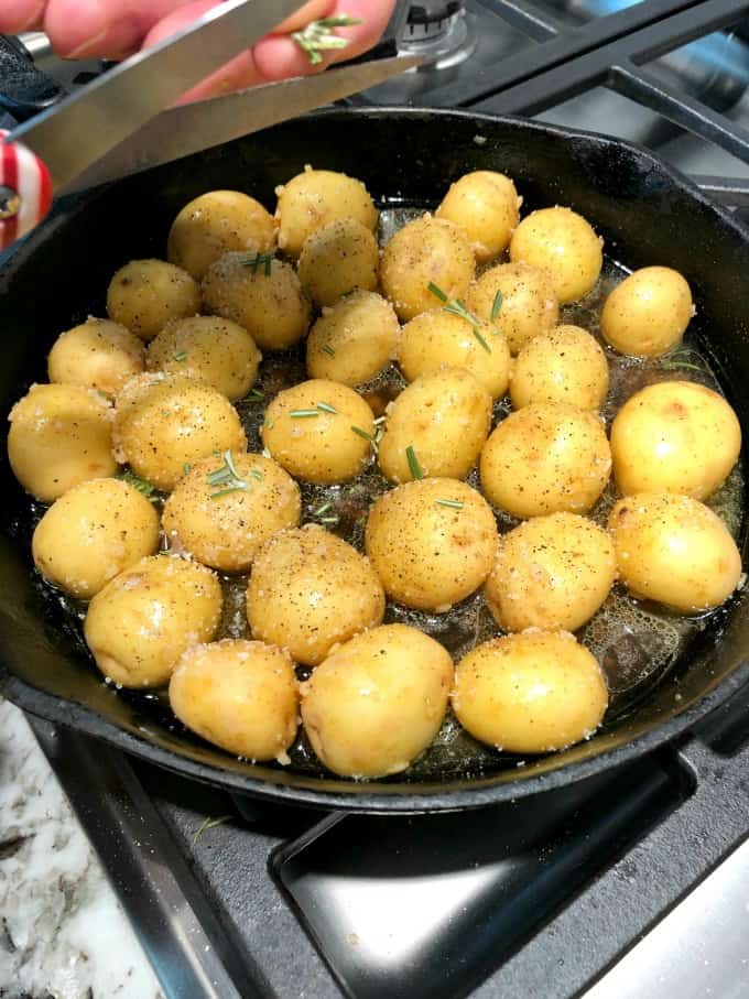 Rosemary being added to a cast iron pan of potatoes