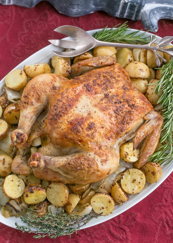 Whole roasted chicken on a platter with potatoes and fresh herbs