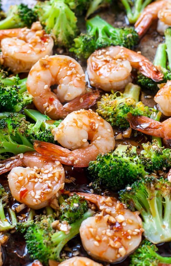 Shrimp and broccoli on a sheet pan with a sauce and sesame seeds