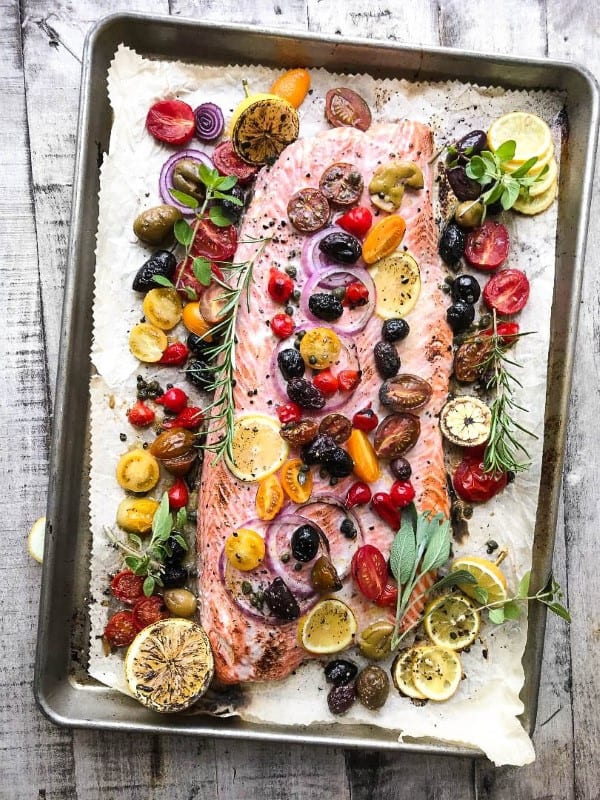 Whole filet of salmon on a sheet pan with olives, tomatoes and herbs