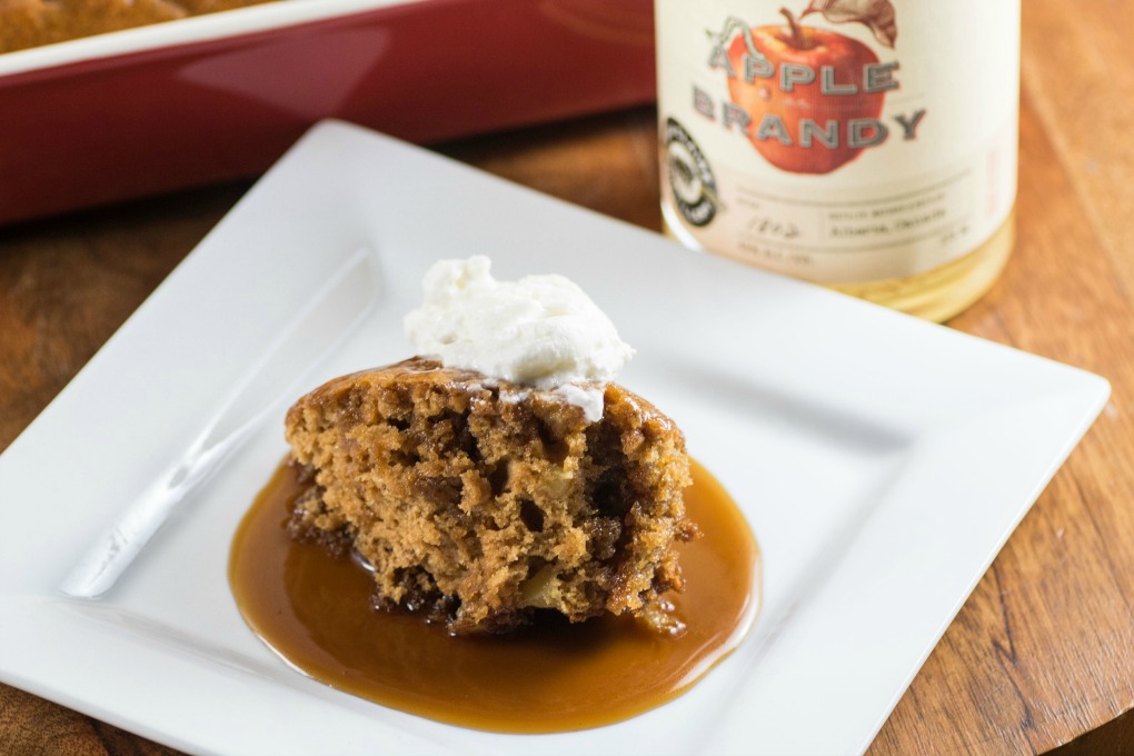 Easy Apple Brandy Sticky Toffee Pudding on a white plate with a bottle of apple brandy