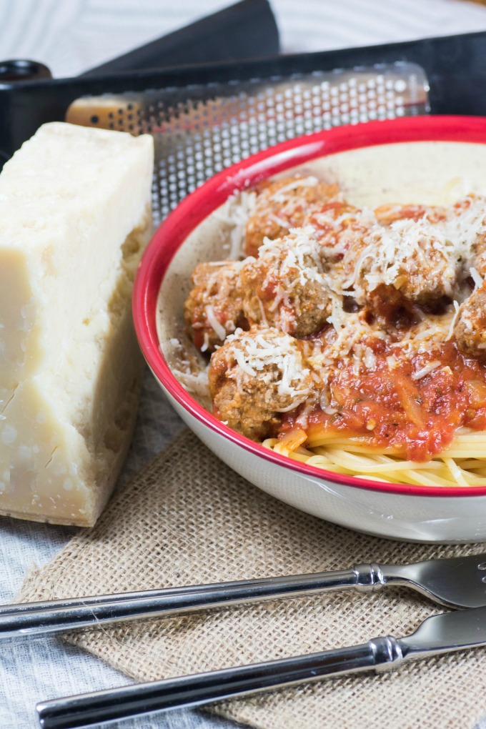 Spaghetti and Meatballs in Marinara Sauce in a bowl with a fork and knife and Parmesan cheese