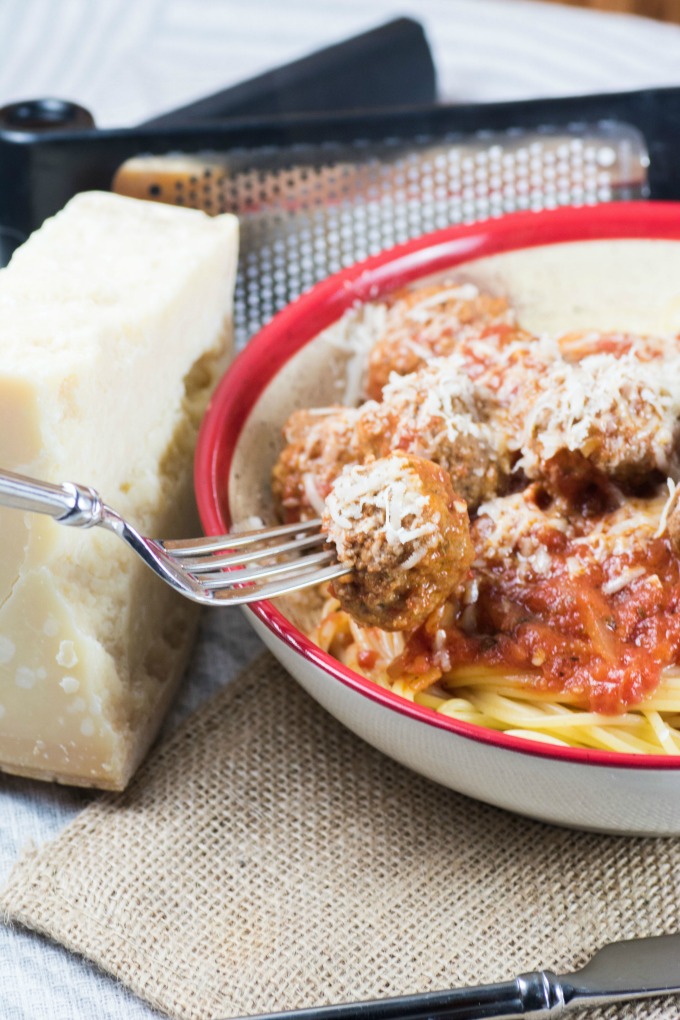 Spaghetti and Meatballs in Marinara Sauce on a fork in a bowl with a block of Parmesan cheese