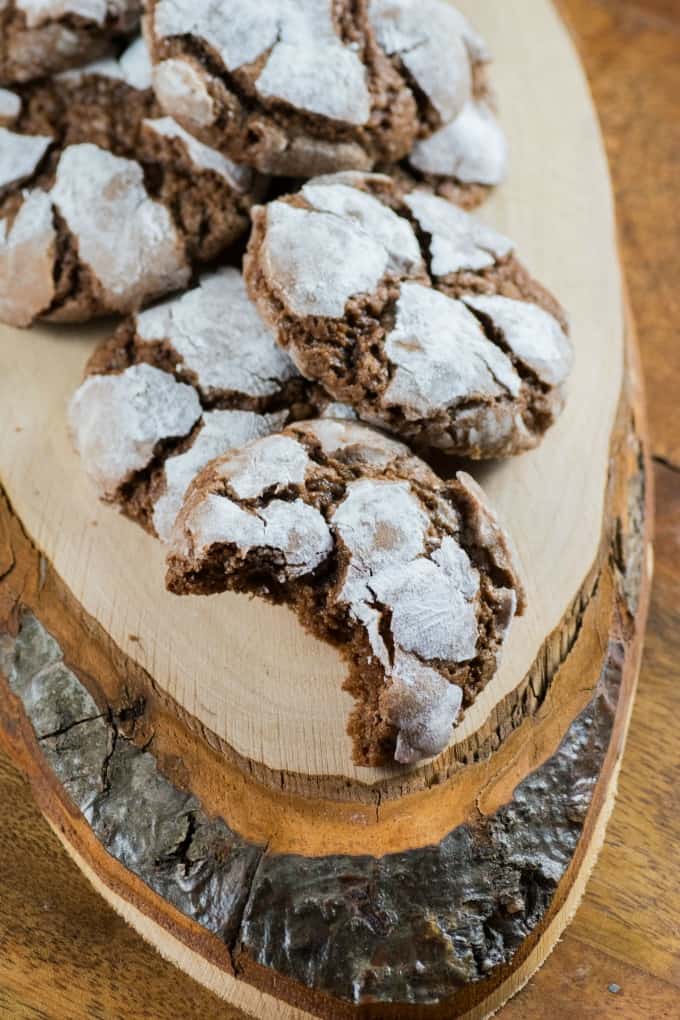 Chocolate Crinkle Cookies on a wooden board, one with a bite taken out. 