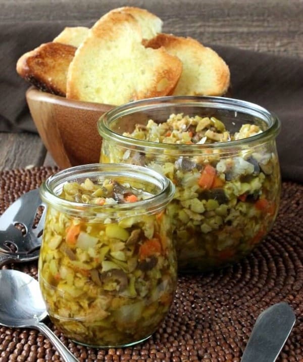 Olive tampenade crostini in a glass jar with the crostini in a wooden bowl 