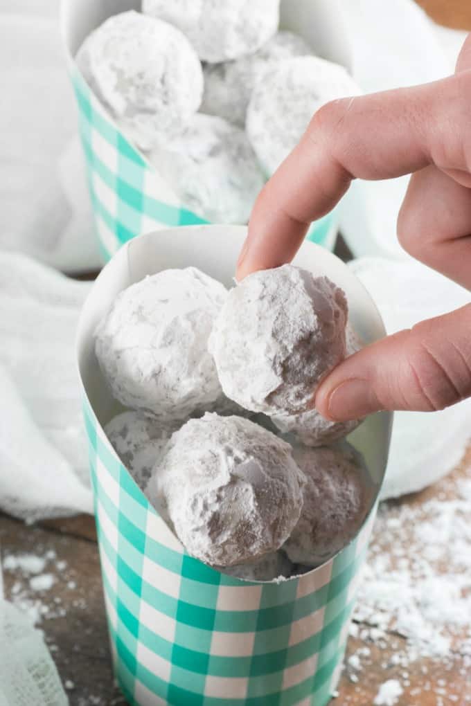 Grabbing a Snowball Cookie from a checkered paper container. 