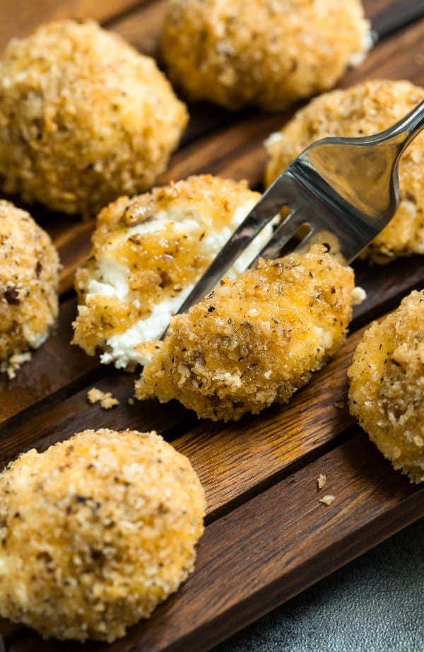 Baked goat cheese balls on a wooden tray with a fork