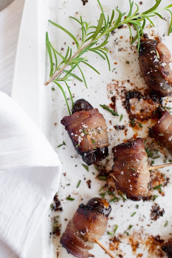 Rosemary bacon wrapped dates on a white serving plate