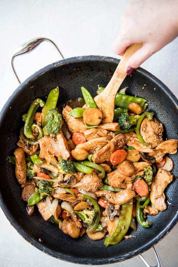 Garlic Sesame Chicken Stir Fry in a skillet being stirred with a wooden spoon