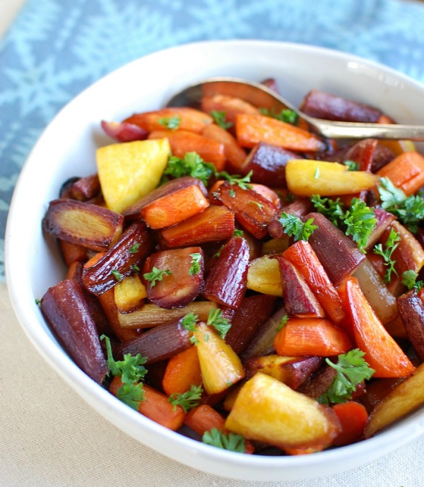 Honey balsamic roasted carrots in a white serving bowl with a serving spoon