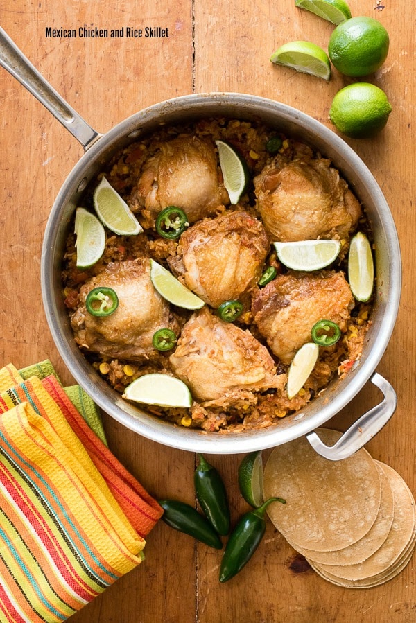 Mexican Chick and Rice In a Skillet with lime wedges and Jalapeno peppers