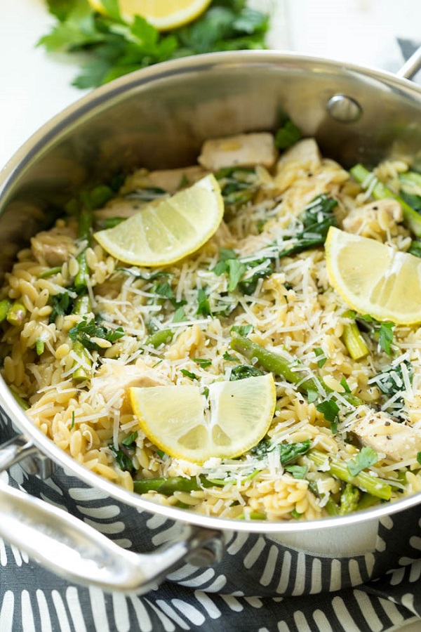 One Pot Lemon Chicken, Spinach, Asparagus with Orzo in a skillet and lemon wedges 