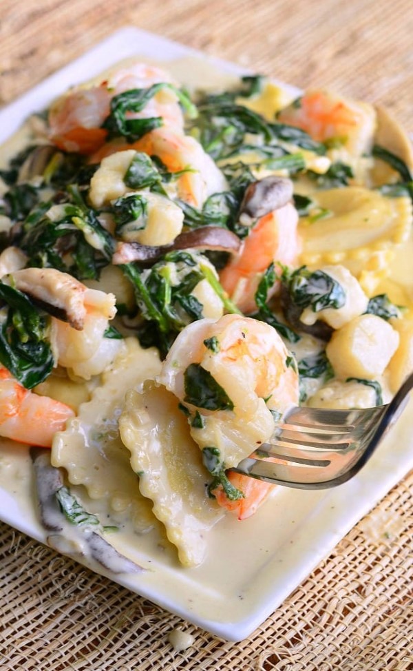 Ravioli with Seafood, Spinach and Mushrooms in a Garlic Cream Sauce on a white plate