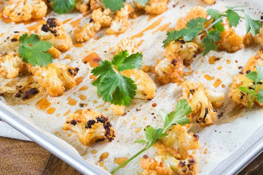 Sweet Sriracha Roasted Cauliflower on parchment paper on a baking sheet with cilantro