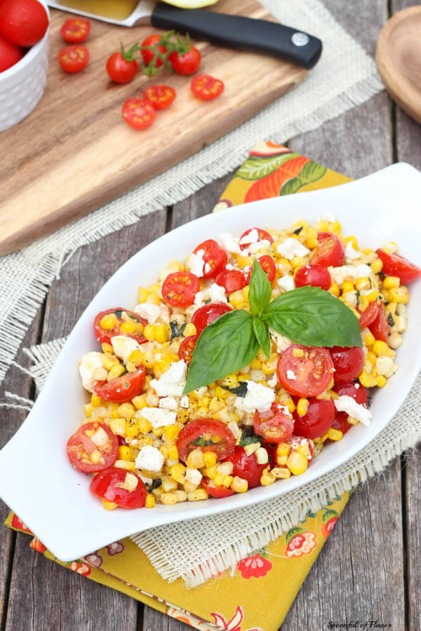 Sauteed corn with tomatoes feta and basil in a white serving dish 