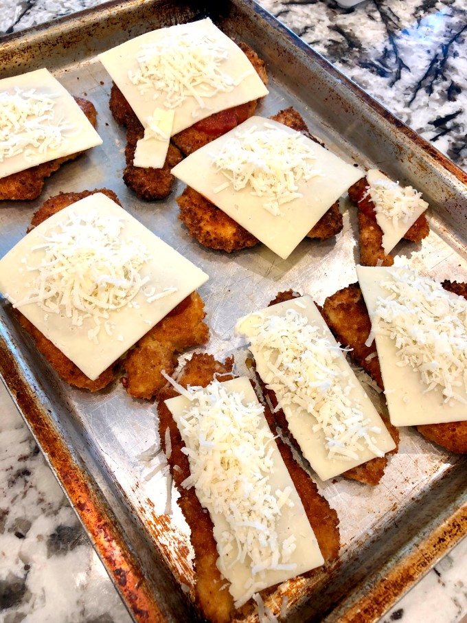 Turkey cutlets on a baking sheet topped with cheese ready for the oven. 