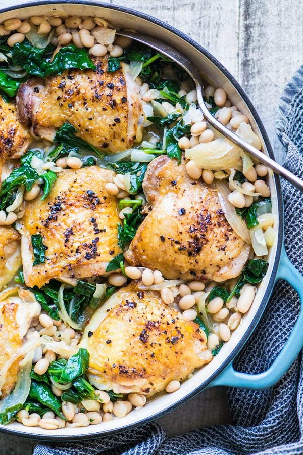 Chicken Thighs With White Beans and Wilted Greens in a skillet with a spoon