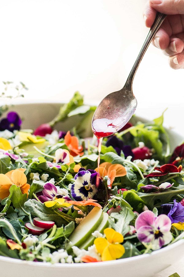 Winter Pansy Salad with a spoon drizzling dressing in a white serving bowl