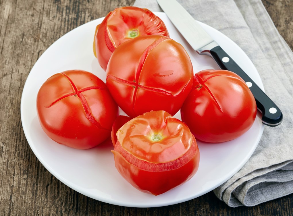 Tomatoes on a white plate with the skins peeling after being boiled.