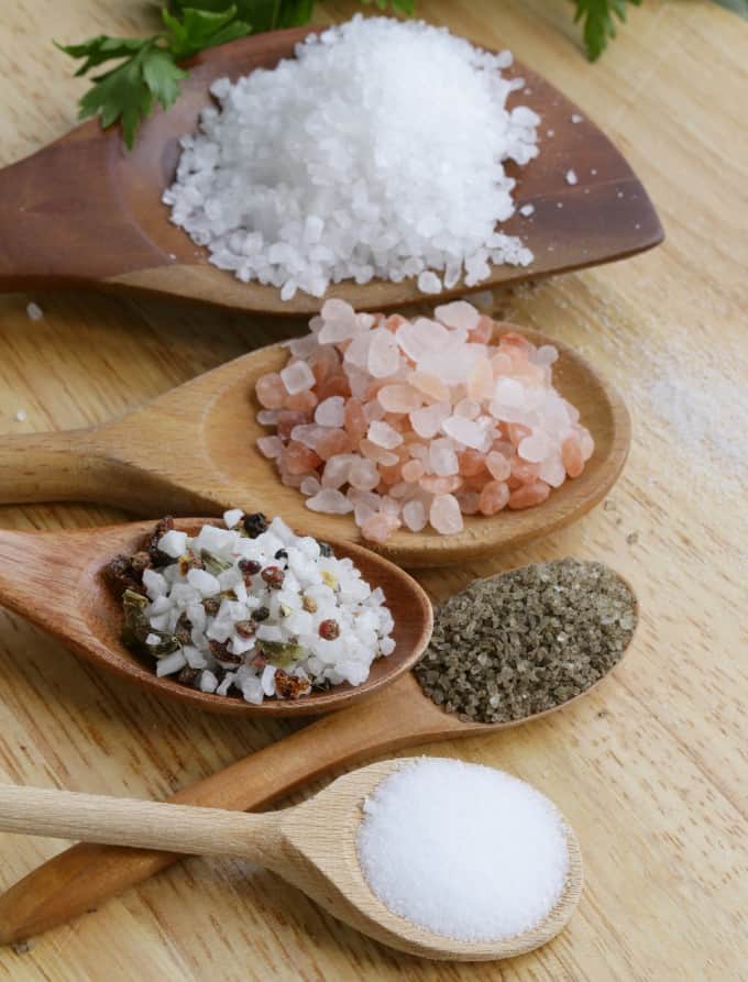 Different types of salts in wooden spoons on a wood board. 