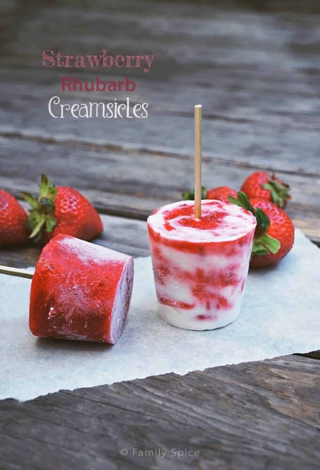 Strawberry Rhubarb Creamsicles on parchment with fresh strawberries.