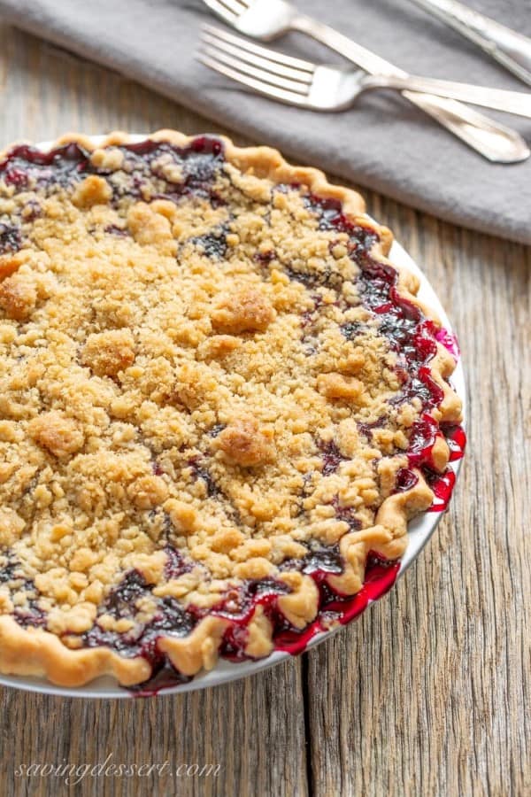 Blueberry Crumble Pie on a wood table with linens and forks