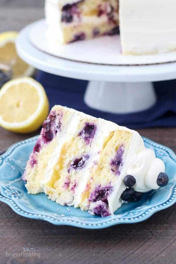 Blueberry Lemon Mascarpone Cake sliced on a light blue plate with the cake in the background