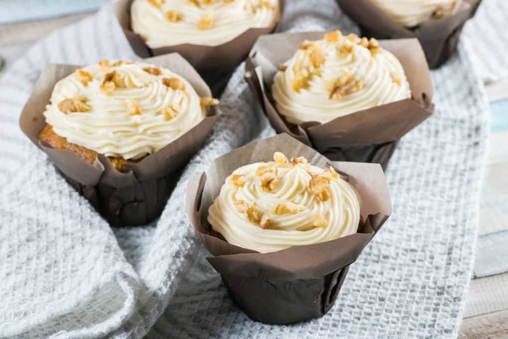 Carrot Cake Cupcakes on a grey and white tea towel on a blueish wooden board. 