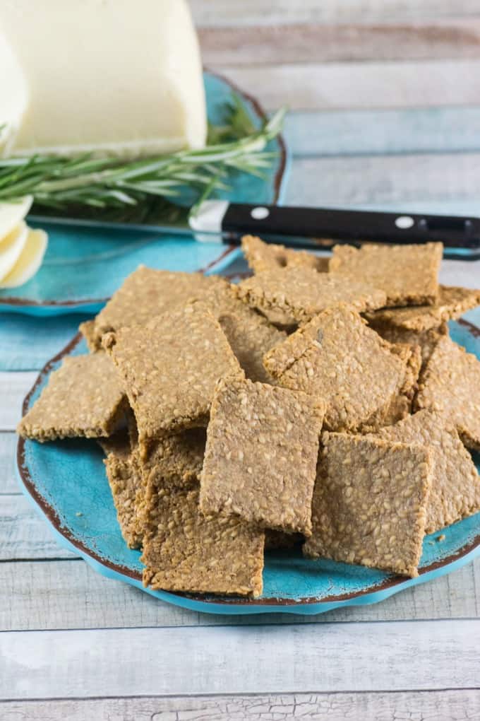 Gluten Free Crackers Recipe on a blue plate with sliced white cheese in the background. 