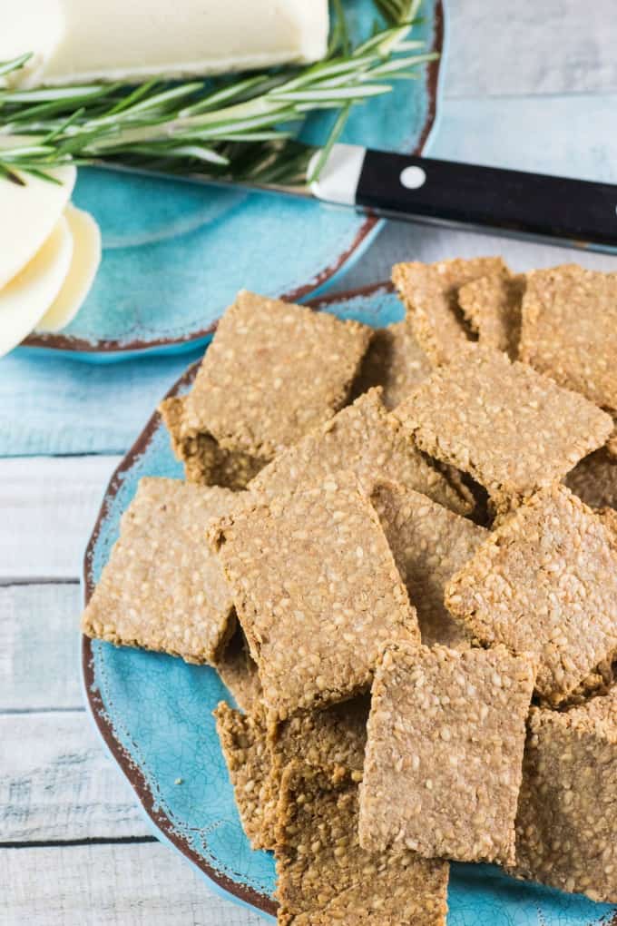 Gluten Free Crackers Recipe on a blue plate with sliced white cheese in the background. 