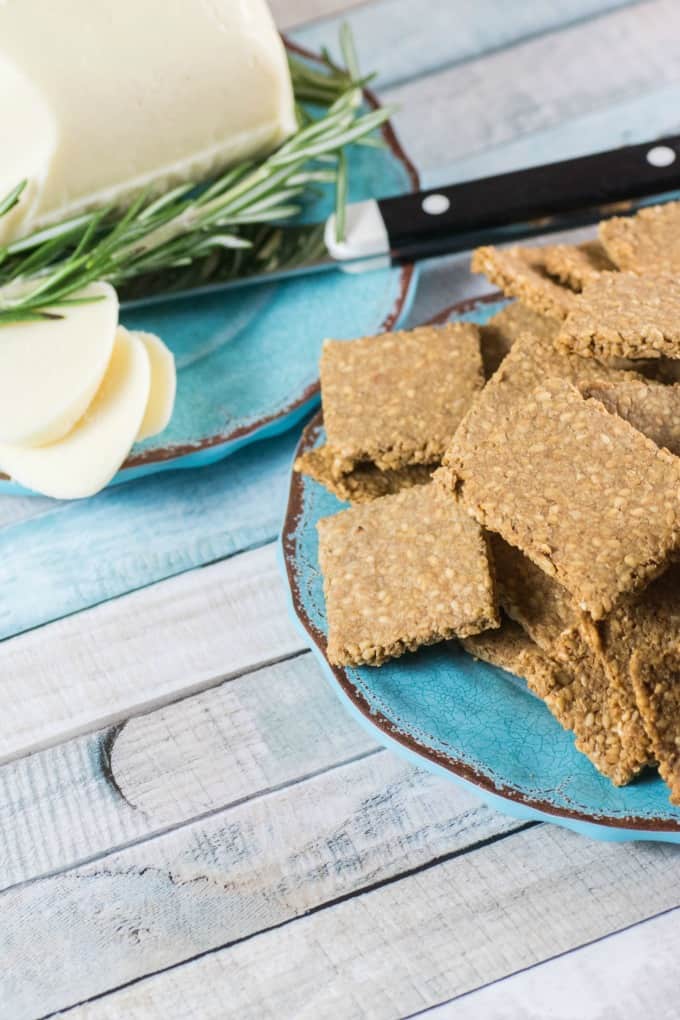 Gluten Free Crackers Recipe on a blue plate with sliced white cheese in the background. 